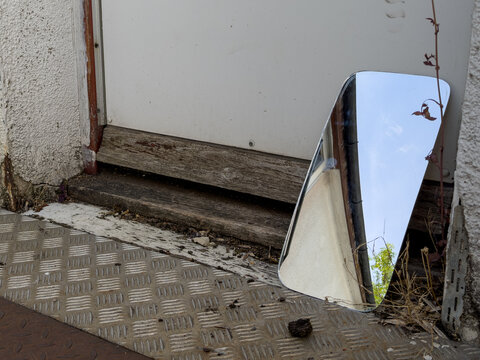 mirror resting against a faded wooden door reflecting the sky above 