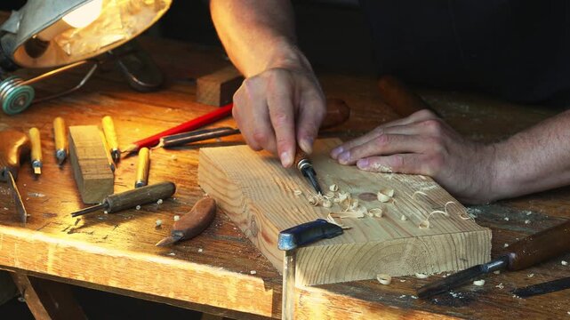 Wood carving tools in craftsman hands during woodwork on workbench. Woodcarving, joinery and timber carpentry desk concept.
