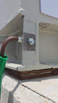 Pan right video of a bare copper grounding wire bolted to a white metal container structure of a 22 kV medium voltage switchgear resting on a concrete base.