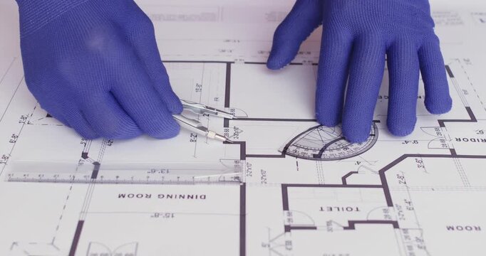A worker takes measurements on a paper plan of a house using a compass and protractor.