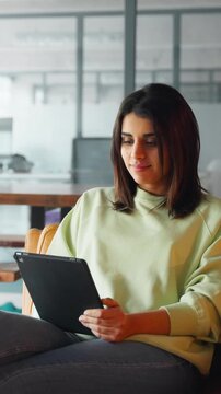 Focused latin young professional business woman girl using pc device computer screen. Female businesswoman in casual clothes sit on sofa holding digital tablet for online work in office. Vertical