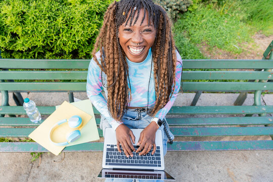 Smiling young woman working on laptop on park bench
