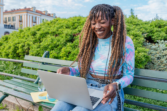 Smiling woman using laptop on park bench outdoors
