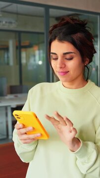 Latin Hispanic female girl student or freelance worker holding smartphone standing in office, looking at camera portrait. Young business woman manager using cell phone mobile app for work. Vertical