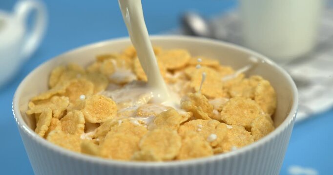Fresh milk pouring into crispy corn flakes in white bowl in ultra slow motion