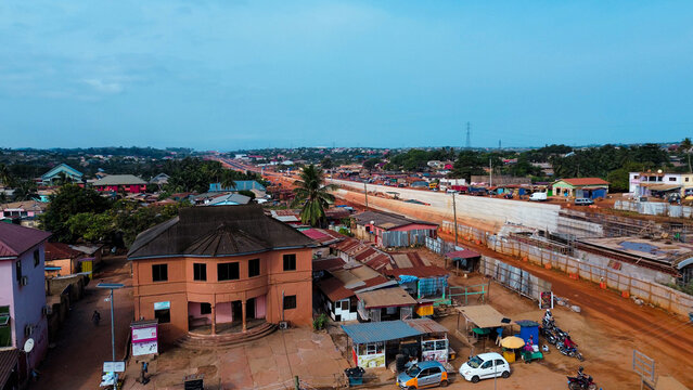 Aerial view of a town in Ghana featuring a prominent orange building, ongoing road construction, residential houses, and local traffic in Kasoa, Central Region, Ghana.
