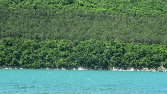 Lush green forest on steep hill above turquoise water of mountain lake. Concept of travel, ecology and pristine wilderness