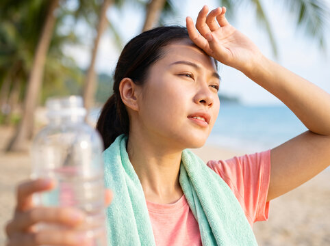 Exhausted asian woman wiping sweat from forehead after workout on the beach