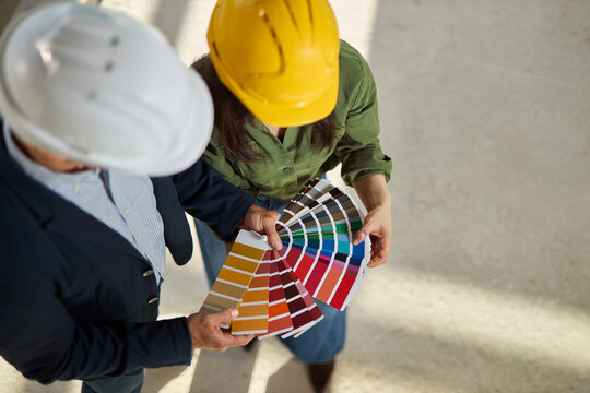 High angle view of an unrecognizable young couple wearing hardhats and holding paint samples at an apartment construction site.