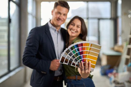 Happy couple holding color swatches and looking at camera at construction site.