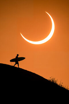 Surfer silhouetted against a solar eclipse at sunset