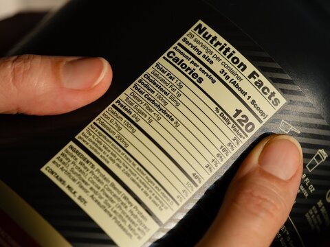 Close-up shot of a black jar of a whey protein powder with nutrition facts label in woman hands.