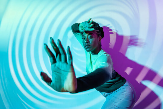 Afro woman dancer posing in neon swirl light studio