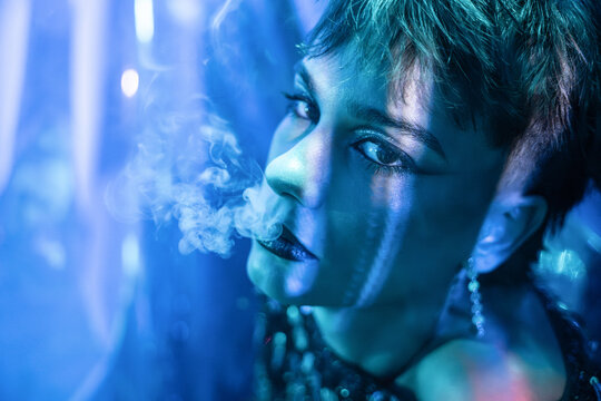 Cyberpunk young woman smoking in neon blue futuristic light
