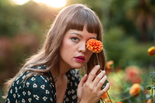 Young woman holding orange flower in sunlit garden