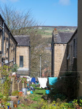 Old fashioned back alley with traditional stone houses with washing hanging from lines and flowers in back yards in Hebden Bridge West Yorkshire