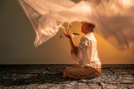 Spiritual Latin woman meditating with lilies in warm light