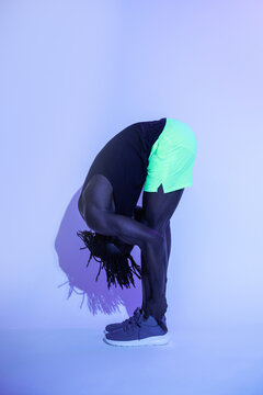 Black athlete bending forward stretching in studio lighting