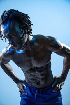 Muscular Black athlete resting in blue-lit studio portrait