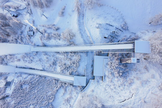 Aerial view of Stadio Olimpico del Salto ski jump facility surrounded by snow-covered trees and winter landscape in Pragelato, Piedmont, Italy.