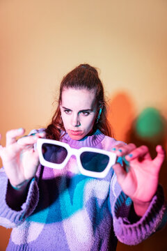 Woman holding white sunglasses in colorful studio light