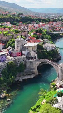 View of Mostar bridge and Neretva River with surrounding historic city and natural scenery.