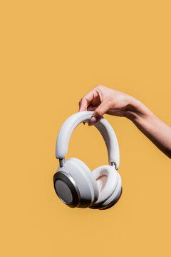 Minimal white headphones held by woman hand on yellow background