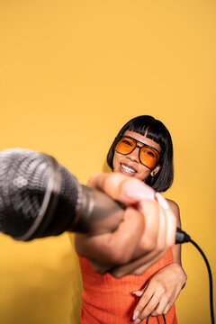 Young Latin woman holding microphone on yellow background