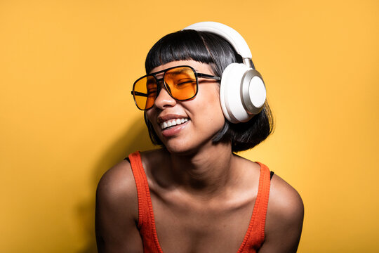 Latin young woman enjoying music with headphones on yellow