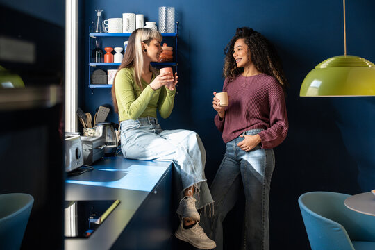 Multiethnic flatmates chatting over coffee in shared kitchen