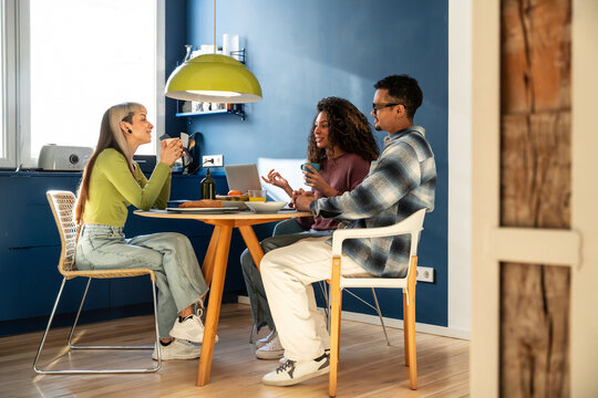 Multiethnic flatmates chatting at kitchen table in home