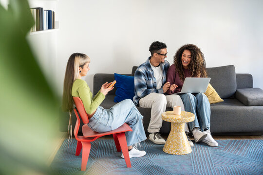 Multiethnic flatmates relaxing with phone and laptop