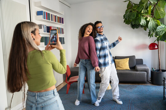 Multiethnic flatmates dancing at home while friend records