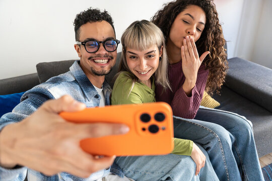 Multiethnic flatmates taking a cheerful selfie on sofa