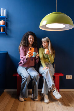 Multiethnic flatmates sharing phone and coffee at home