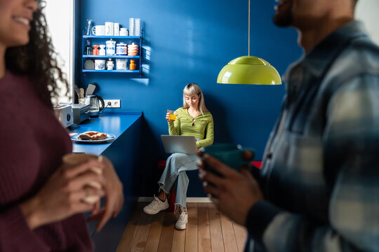 Multiethnic flatmates relaxing in blue kitchen with coffee