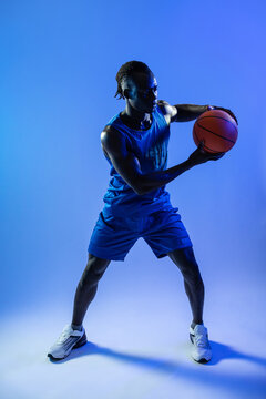 Black basketball player holding ball in blue studio light