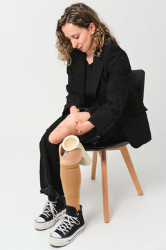 Woman with prosthetic leg adjusting stump and sock in studio
