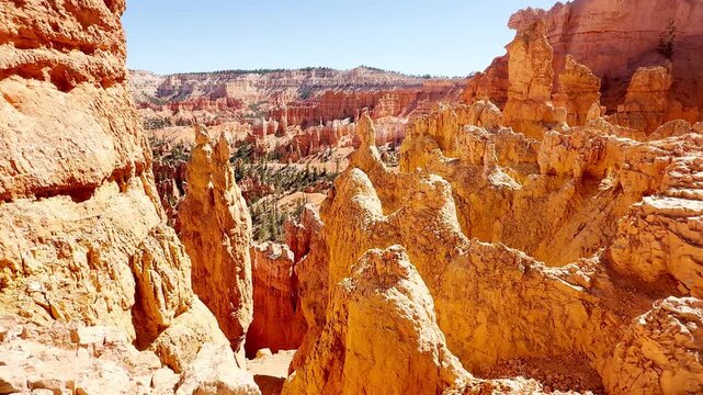 A smooth cinematic low angle shot panning across unique red rock spires resembling chess pieces or statues in Bryce Canyon, Utah. Scenic hiking trails and rare pine trees under a clear blue sky.