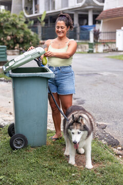 Woman throwing dog waste bag in trash bin with husky