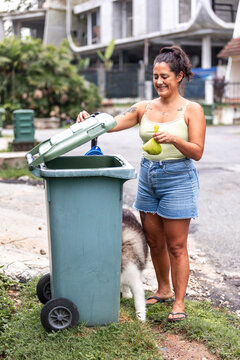 Woman holding dog waste bag beside trash bin outdoors