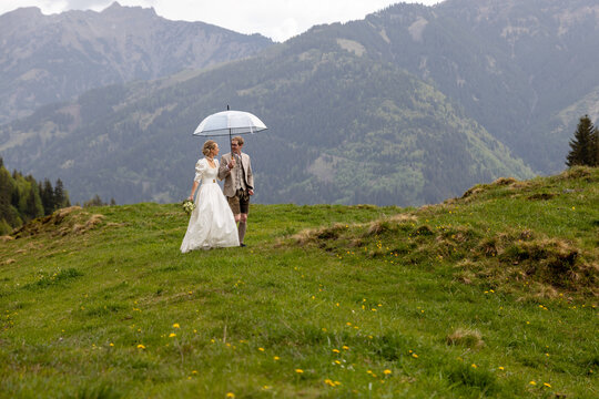 Bride and groom with umbrella in Austrian alpine meadow