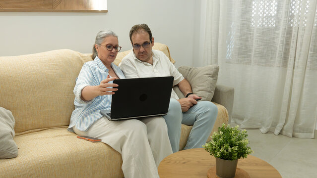 Senior couple using laptop together on living room sofa