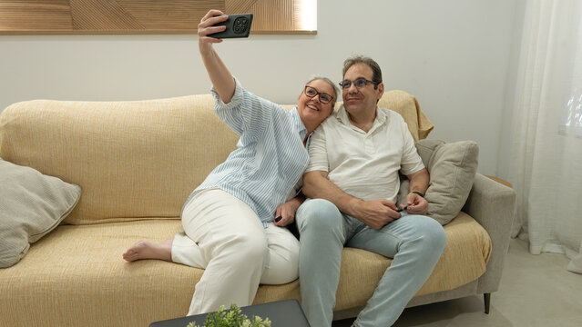 Senior couple taking a selfie together on living room sofa