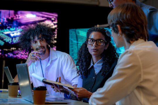 Low-light scene where a curly-haired engineer and a curly-haired developer smile over a solution together in a modern technology office bathed in blue light, highlighting (frame 318)
