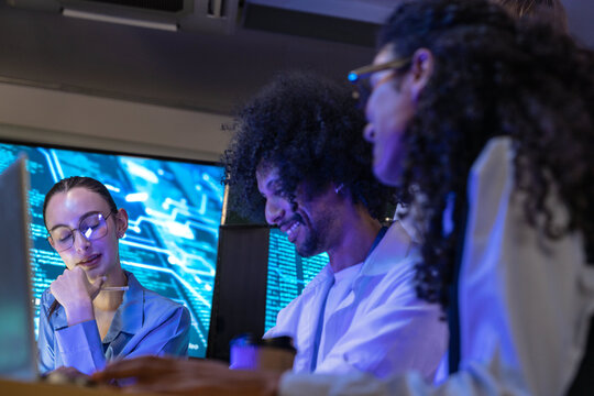 Close view of a diverse, multiethnic software team share a screen in the purple light in a modern technology office bathed in blue light, capturing collaboration on an inclusive (frame 513)