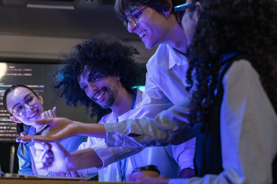 Close view of a diverse, multiethnic software team examine a glowing device together in a modern technology office bathed in blue light, reflecting diversity and innovation in a (frame 544)