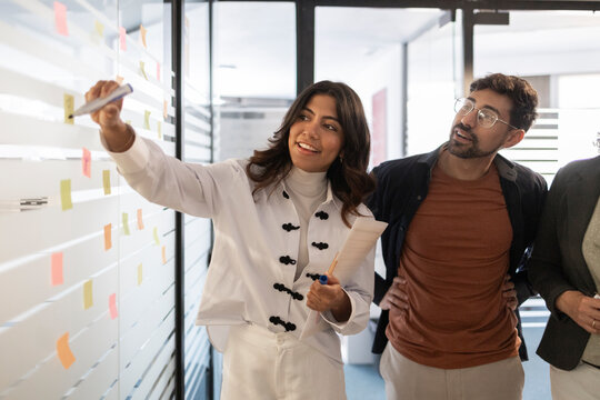 Coworking team brainstorming ideas on office glass wall