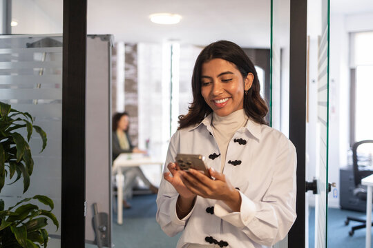 Smiling professional using smartphone in modern office hallway