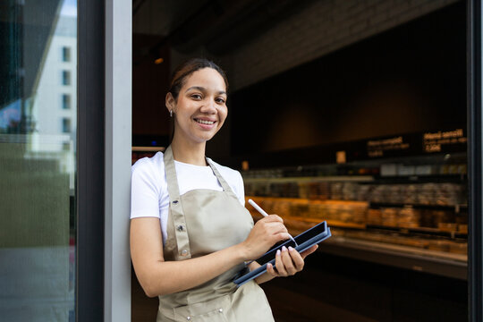 Smiling cafe worker using tablet at entrance